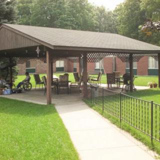 A gazebo with patio furniture set on a grassy lawn, surrounded by trees and buildings.