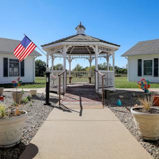 A charming gazebo adorned with an American flag, surrounded by beautifully landscaped homes under a clear blue sky.
