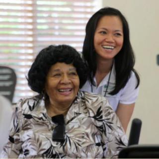 An elderly woman and her caregiver smiling together indoors.