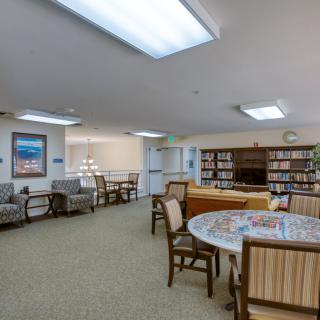 A cozy library interior with bookshelves, comfortable chairs, and a round table under fluorescent lighting.