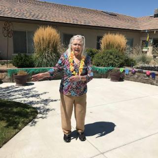 An elderly woman enjoys a sunny day in her colorful outfit, surrounded by a serene garden.