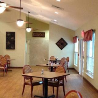 A well-lit dining area with neatly arranged tables and chairs, complemented by decorative wall art and large windows.