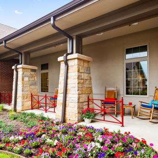 A cozy outdoor porch with chairs and a vibrant garden filled with colorful flowers.