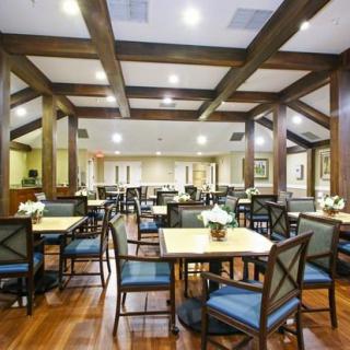 A spacious dining room with wooden beams, neatly arranged tables and chairs, and warm lighting.