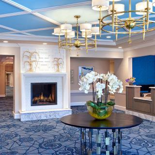 A luxurious hotel lobby featuring a fireplace, elegant chandeliers, and a central table with orchids.
