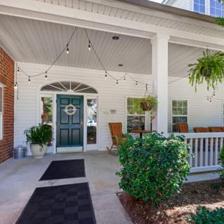 A welcoming porch with a blue door, string lights, and outdoor seating surrounded by greenery.