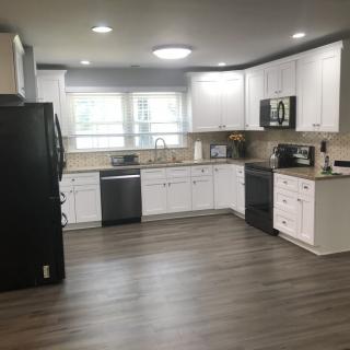 A modern kitchen with white cabinets and wood flooring, featuring various appliances.