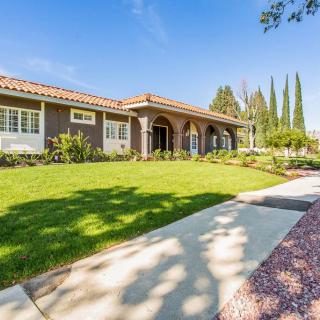 A spacious suburban house with a well-maintained front lawn and surrounding greenery on a sunny day.