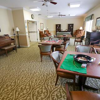 A cozy living room with multiple tables and chairs, a piano, and decorative carpet.