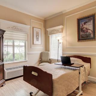 A cozy hospital room featuring a comfortable bed, natural light from the window, and decorative art.