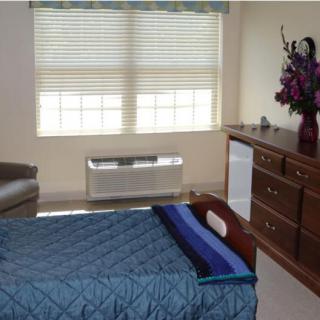 A cozy bedroom with a blue bedspread, a dresser, and a window letting in natural light.