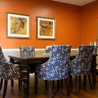 A stylish dining room with a dark wooden table and patterned chairs, complemented by an orange accent wall and framed artwork.