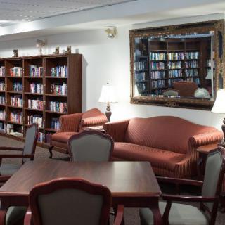 A cozy library space featuring bookshelves, a sofa, chairs, and a large wall mirror.