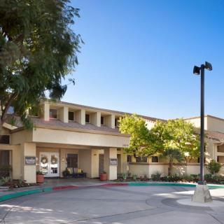 A commercial building entrance with a surrounding parking lot and trees under a clear blue sky.