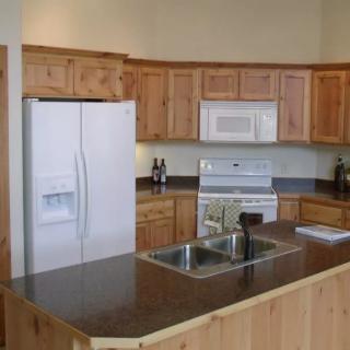 A modern kitchen featuring wooden cabinets, a granite countertop, and essential appliances such as a refrigerator and oven.