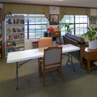 A library room with a table and chairs, bookshelves, and a plant near the windows.