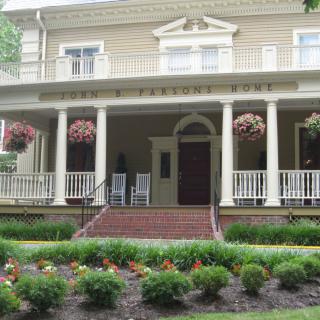 A large house with a spacious porch, surrounded by a well-maintained garden and hanging plants.