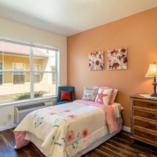 A cozy bedroom with a single bed, decorated in warm colors, featuring floral artwork and a wooden nightstand.