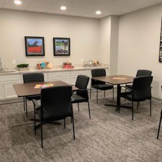 A neatly arranged meeting room with tables and chairs, featuring wall art and a carpeted floor.