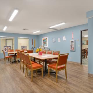 A well-lit dining room with blue walls, featuring a large table surrounded by orange chairs.