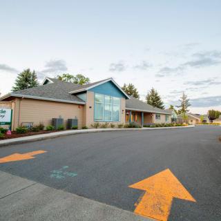A modern building with a parking lot featuring directional arrows, surrounded by trees under a cloudy sky.