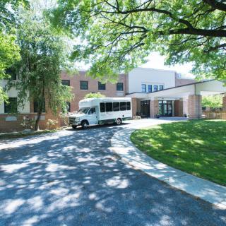 A building with a driveway and a bus parked under the shade of trees.