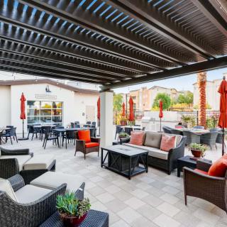A modern outdoor patio with comfortable seating under a pergola, featuring tables and red umbrellas.