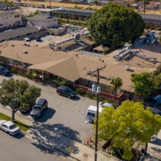 Aerial view of a suburban area with a building and parking lot surrounded by trees and parked cars.