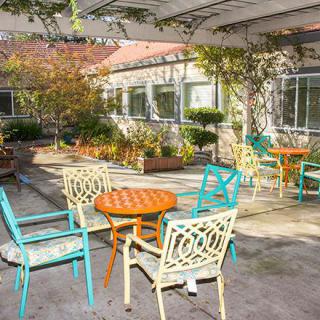 A sunny patio with colorful tables and chairs surrounded by a garden.