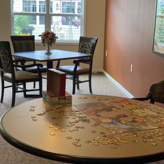 A cozy room featuring a table with an incomplete puzzle and a dining set by the window.
