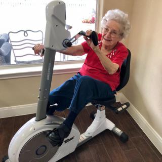 An elderly woman using an exercise bike indoors.