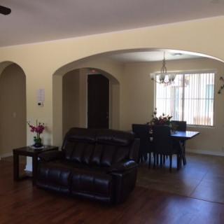 A cozy living room and dining area with archways, featuring dark leather furniture and wood flooring.