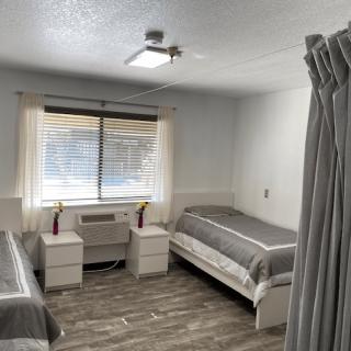 A minimalist bedroom with two single beds, nightstands, and an air conditioner beneath a window.