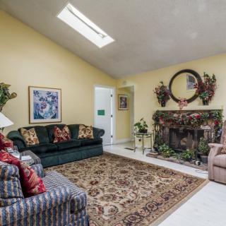 A cozy living room featuring a fireplace, colorful sofas, and a patterned carpet beneath a skylight.