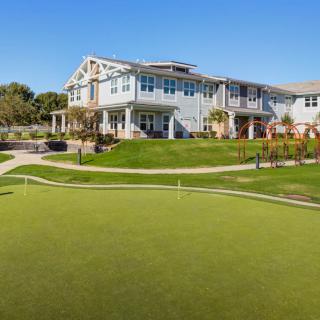 A clubhouse overlooking a green golf course under a clear blue sky.