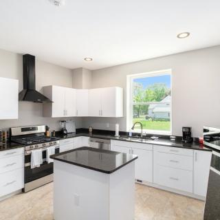 A modern kitchen with white cabinets, a central island, and stainless steel appliances, illuminated by natural light from a large window.