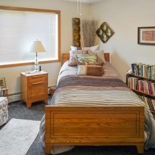 A cozy bedroom with a single wooden bed, a nightstand with a lamp, and a bookshelf filled with books.