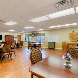 A well-lit dining area in a senior living facility with multiple tables and chairs.