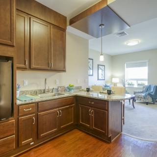 A modern kitchen with wooden cabinets and an open layout leading to a living area.