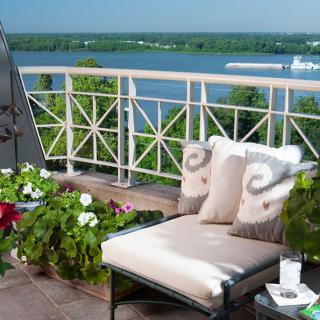 A comfortable balcony with a lounge chair overlooking a scenic river view, surrounded by green plants.
