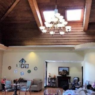 A cozy living room with a high wooden ceiling and skylights, featuring a chandelier, seating area, decorative plates on the wall, and a fireplace.