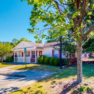 A charming residential home with a welcoming front porch set in a sunny, green environment.