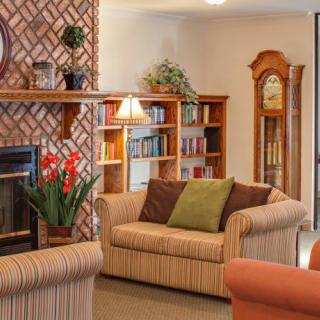 A cozy living room with comfortable sofas, a fireplace, bookshelves, and a grandfather clock.