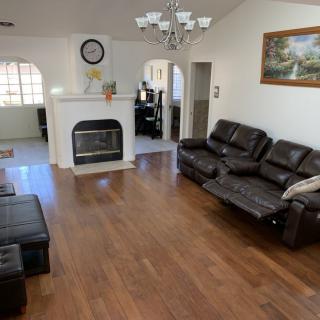 A spacious living room with hardwood floors, featuring a leather sofa, a fireplace, and a chandelier.
