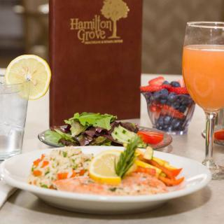 A gourmet meal featuring salmon with vegetables, a fresh salad, and a mixed fruit bowl at Hamilton Grove restaurant.
