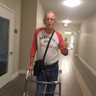Person using a walker gives a thumbs up in a hallway.