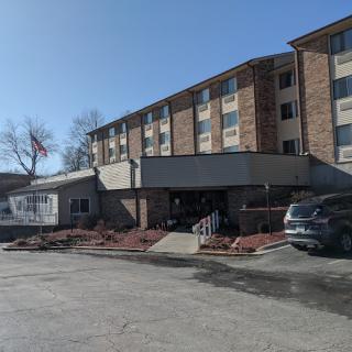A view of a multi-story apartment building with cars parked in front on a clear day.