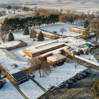 Aerial view of snow-covered buildings surrounded by trees in a rural winter landscape.