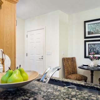 A cozy kitchen space with a bowl of pears on the counter and a small dining area with artwork on the wall.