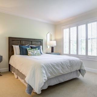 A cozy bedroom with a neatly made bed, soft lighting, and large windows.